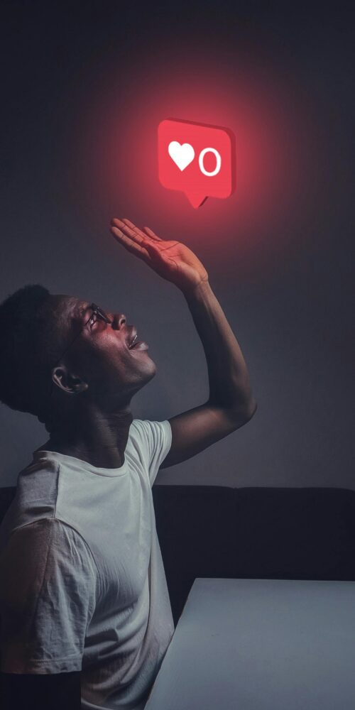 A man sits indoors reaching towards a glowing social media notification icon.